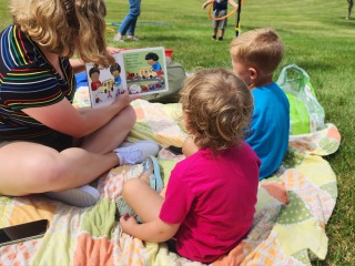 college student reading to two young children outside 