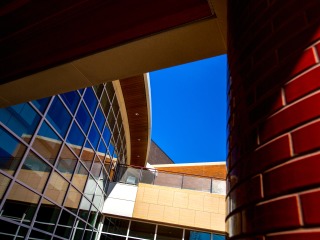 An abstract angle of the Joe Rosenfield Center. On the left, a glass, gridded wall and on the right, a close up of a red bricked pillar.