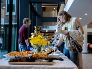 one person serving food and the other getting it with yellow flowers in the background 