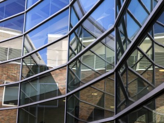 Wall-to-wall windows in the Noyce Science Center's courtyard reflect a blue sky.
