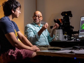 A professor and a male student discuss fluorescent microscopy images pulled up on a laboratory computer.