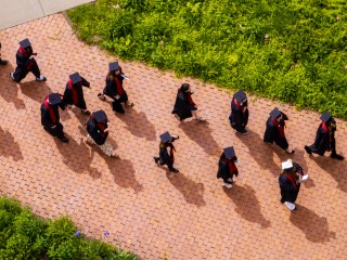 Aerial view of students in graduation gowns and caps walking down a cobblestone path 