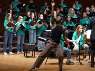 A young man performs an interpretive dance while a choir performs.