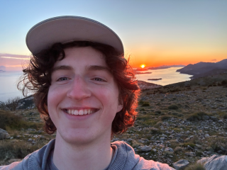 Ben smiles with a beautiful sunset and landscape behind him