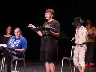 Five students on a dark stage holding black binders