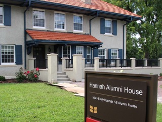 Hannah Alumni house, a grey house with dark blue trim and red tile roof. In the foreground is the entrance sign with the full name Mary Emily Hannah 58 alumni house