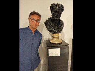 Professor Joe Neisser standing next to a black stone bust