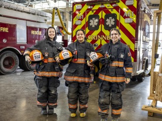 Three students with fire equipment on and ambulance behind them. 