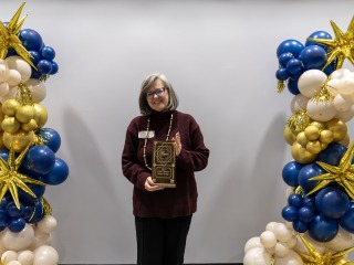 President Harris Holding an award with blue and yellow balloons on side 