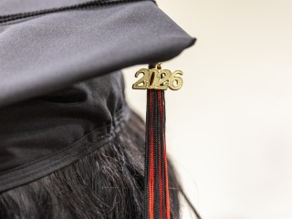 A close up of a mortarboard cap with a red and black tassel and a '2026' charm