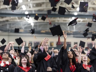 Students wearing black and red graduation regalia throw their caps in the air