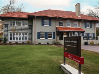 A two story stucco house with a red tile roof has a sign proclaiming it Hannah Alumni House 1527 Broad St