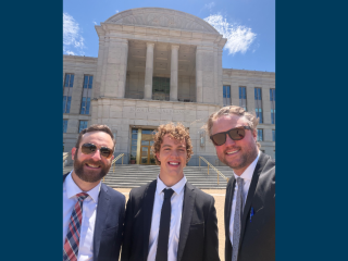 three people in front of building with blue sky 