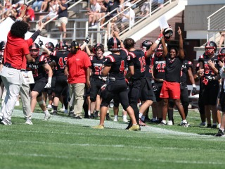 Players and coaches cheer on the sidelines during a football game.