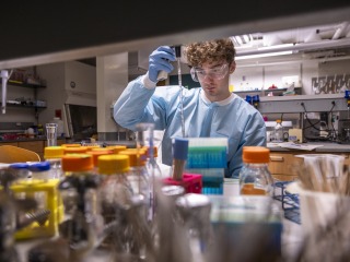 A young man in laboratory garb works with soil samples in a lab.