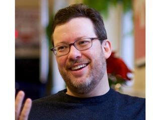 Close-up of the face of a smiling man with glasses and a dark-colored shirt. The man pictured is Sean Forman, President of Sports Reference LLC.