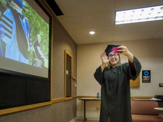 Lexy Greenwell waves at President Kington through the phone, President on screen in background
