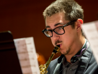 Man blowing into instrument with music scores on stands in the foreground