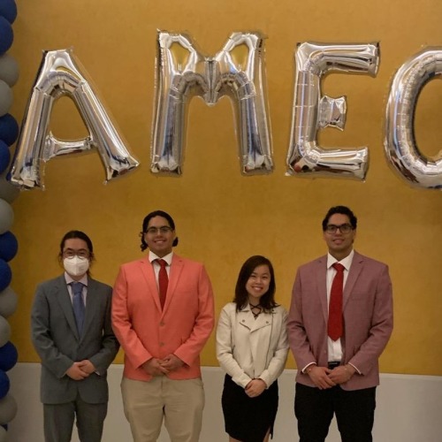 Four students with the AMEC balloon arch at the conference entrance.