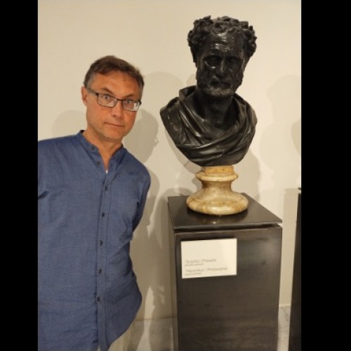 Professor Joe Neisser standing next to a black stone bust