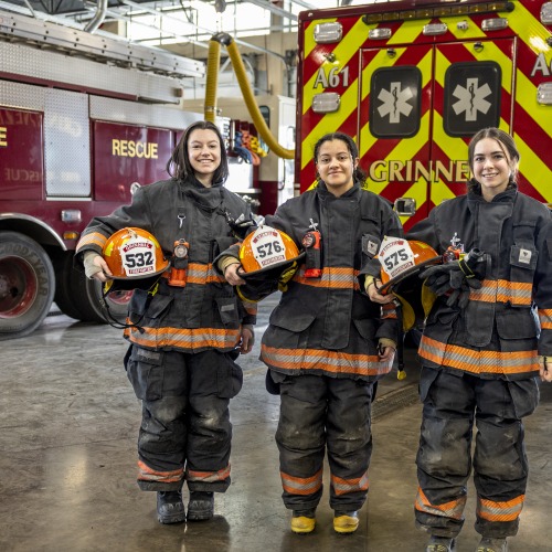 Three students with fire equipment on and ambulance behind them. 