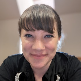 A woman with brown hair in a ponytail. She is wearing a black top. 