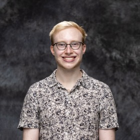 A headshot of Oliver Schoenborn in a short-sleeved white floral button-up.