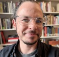 Portrait of a white transgender professor in front of his bookshelf