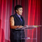 Photo of Valeriya Woodard '25 giving a speech with a deep red backdrop. 