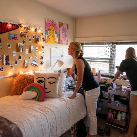 Two students decorate a dorm with pictures and twinkle lights