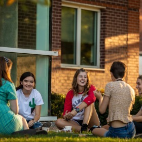 Students sitting together on the ground outside of a dorm room