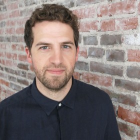 man standing in front of a brick wall