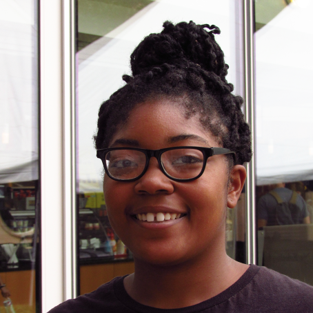 A girl with glasses smiles. Her hair is braided and pulled into a bun.
