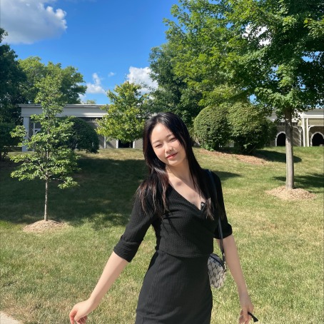 A girl wearing a black dress is standing in a park on a sunny day.