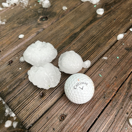 Three hailstones and a golfball on a wooden deck. The hail is the same size and color as the golfball.