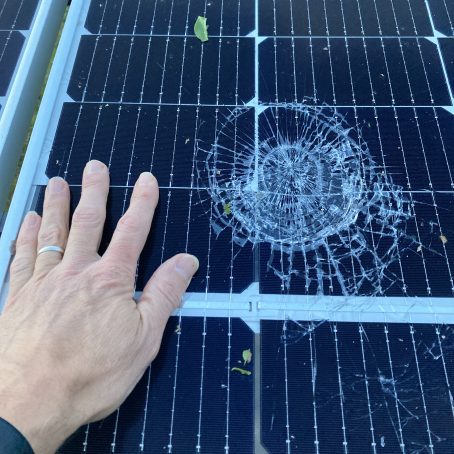 A solar panel with a shattered circle. A man's hand is placed next to the crack for comparison.