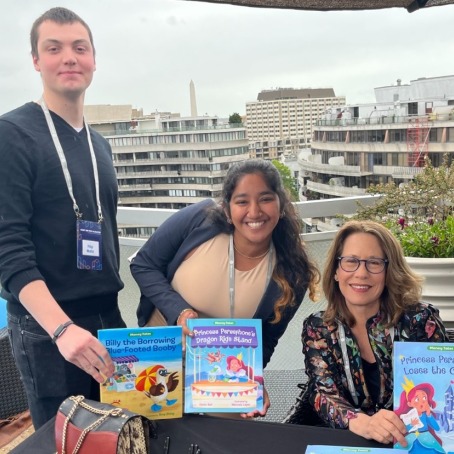 Matic, Manchanda, and an author of children’s books show off three book covers. 