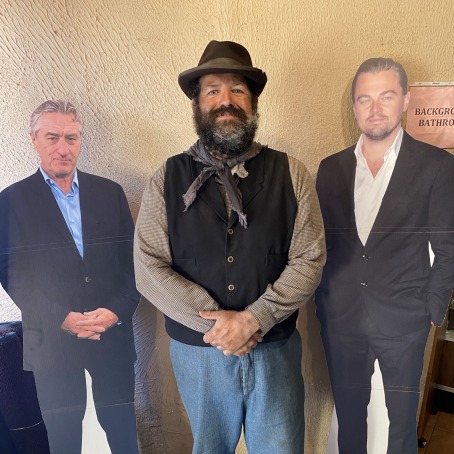 A man in a vest, brown-tatted hat, and blue jeans poses in between a Leonardo DiCaprio and Martin Scorsese cutouts.