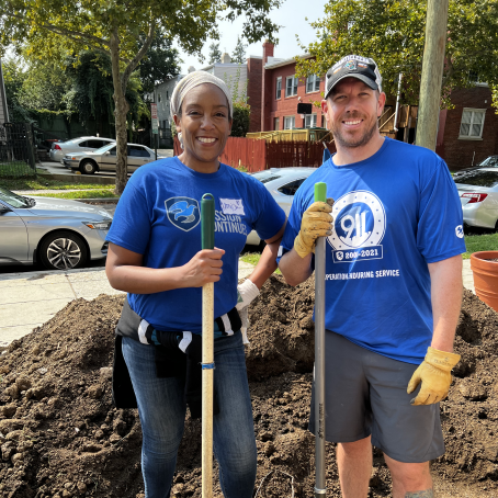 Monica standing with another person with shovel and dirt below them
