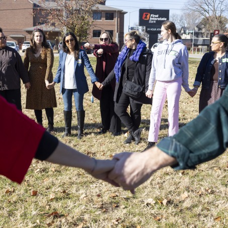 A group of adults stand in a circle with hands clasped