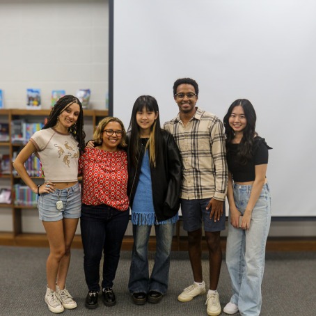 Five college students standing with their arms around each other smiling