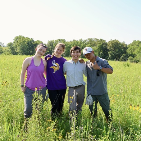 Four Grinnell College Students standing in the prairie at the Grinnell College's Conard Environmental Research Area.