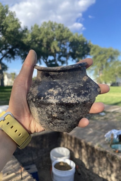 A hand holds a small Chinese brown glazed stoneware shouldered jar fragment recovered from the dig site.
