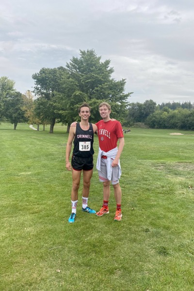 Two young men, one in a cross country uniform, pose on the cross country course