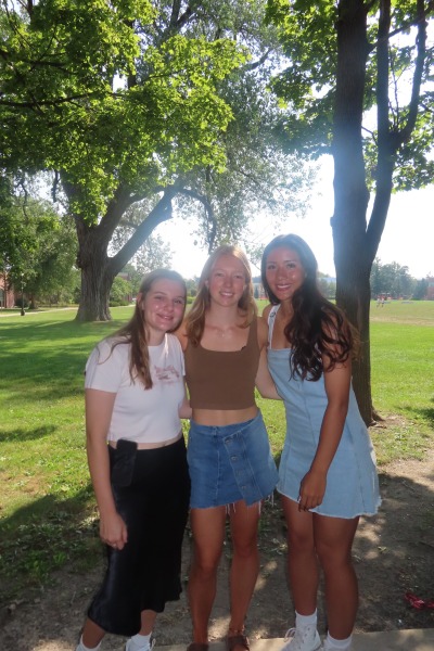 Three young women pose against a lush green campus backdrop