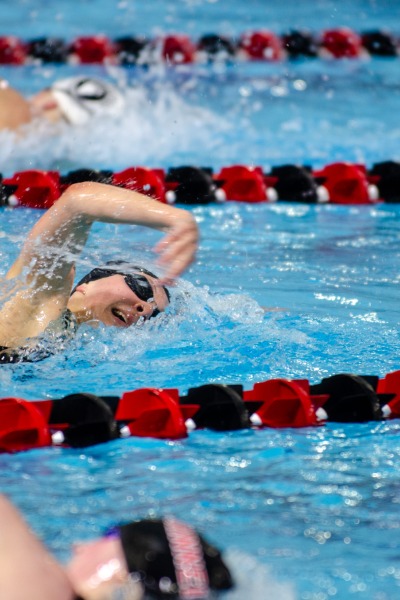 Three women swimming freestyle in a pool with black and red lane dividers