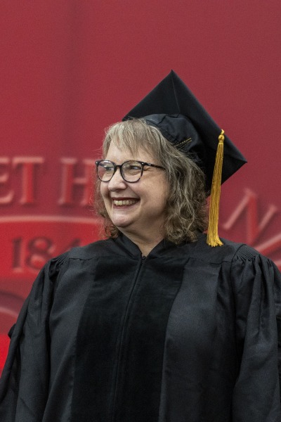 Valerie Schrag waring black graduation regalia in front of a red background