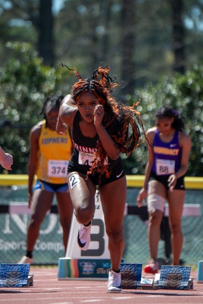 A female track runner in a black uniform takes off from starting blocks